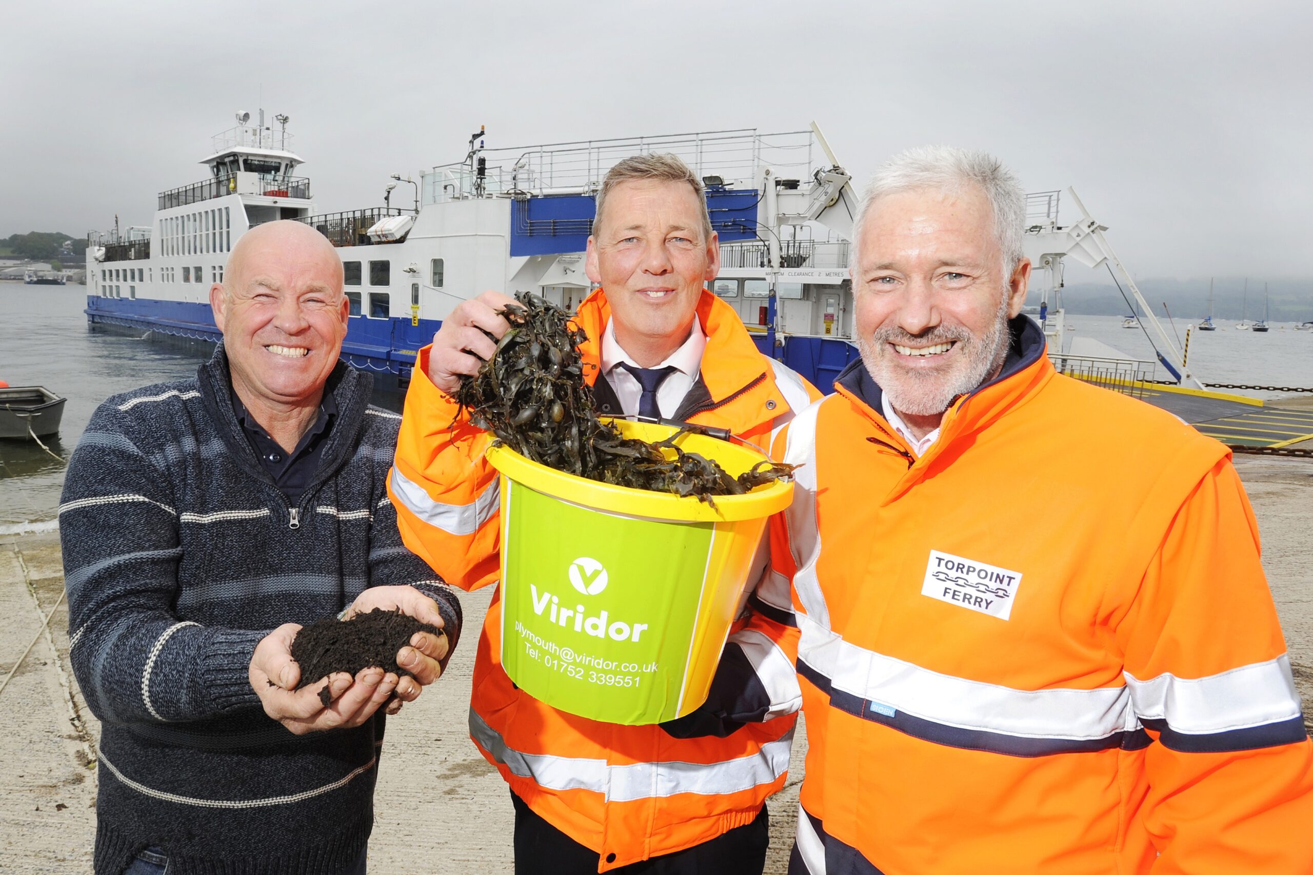 3 people posing with seaweed in a bucket in front of a Torpoint Ferry