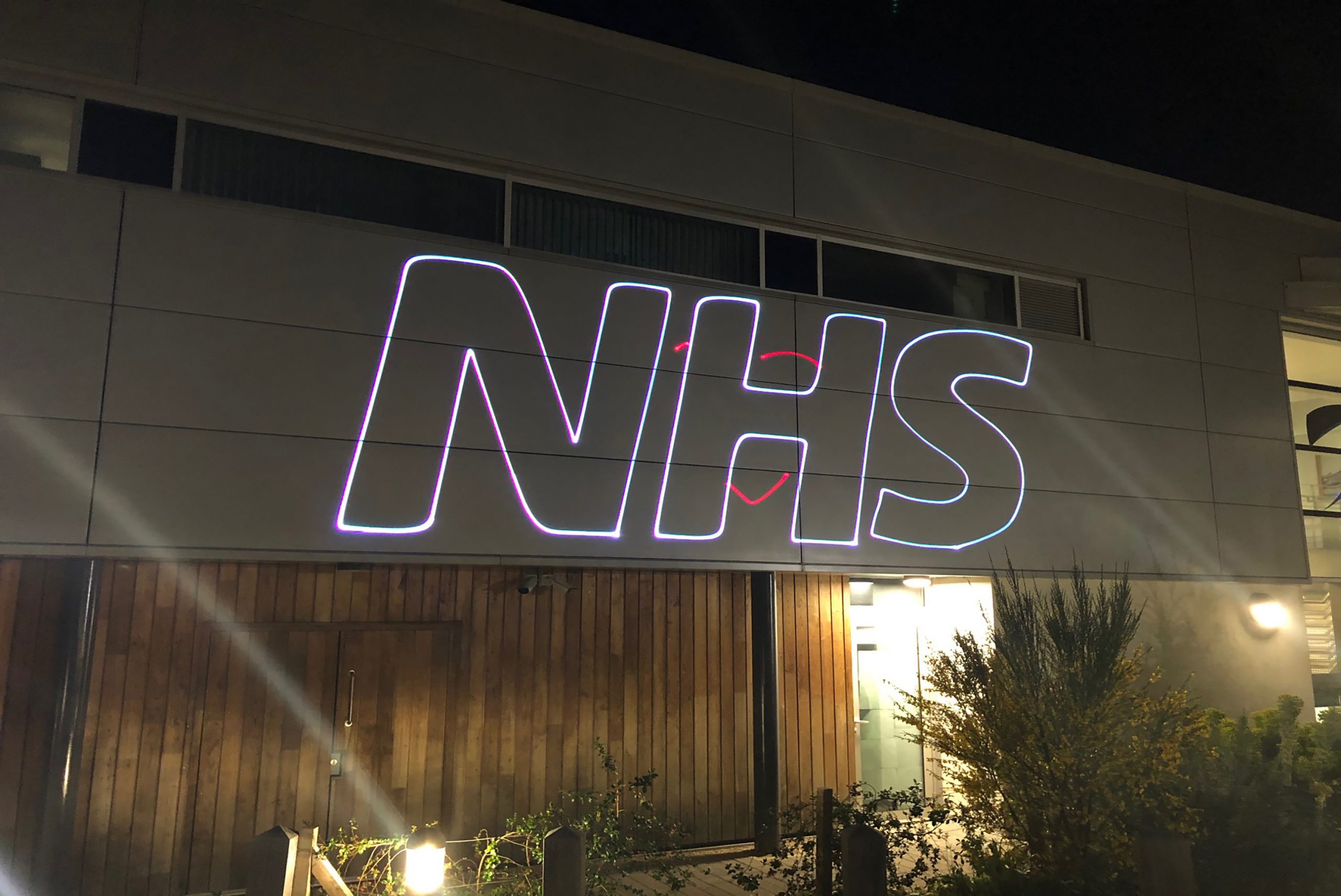 A photo of a laser projecting the NHS logo on the side of the Tamar Crossings building